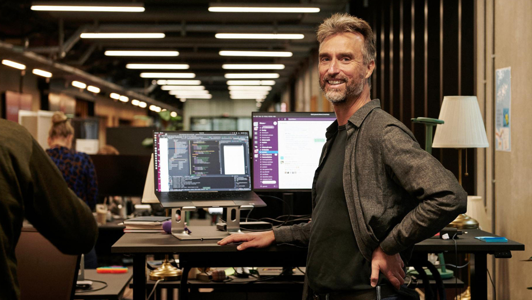 Person stood at a computer desk smiling at camera